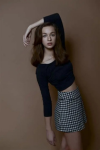 Young woman posing in stylish casual outfit with navy top and patterned skirt against neutral background